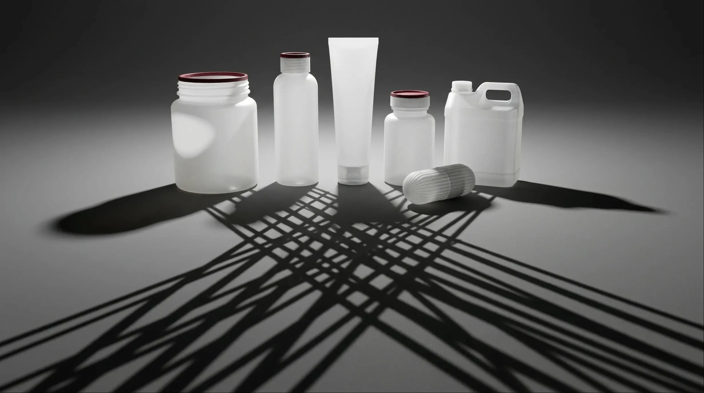 Translucent white containers of varying shapes, their cast shadows crossing in the foreground