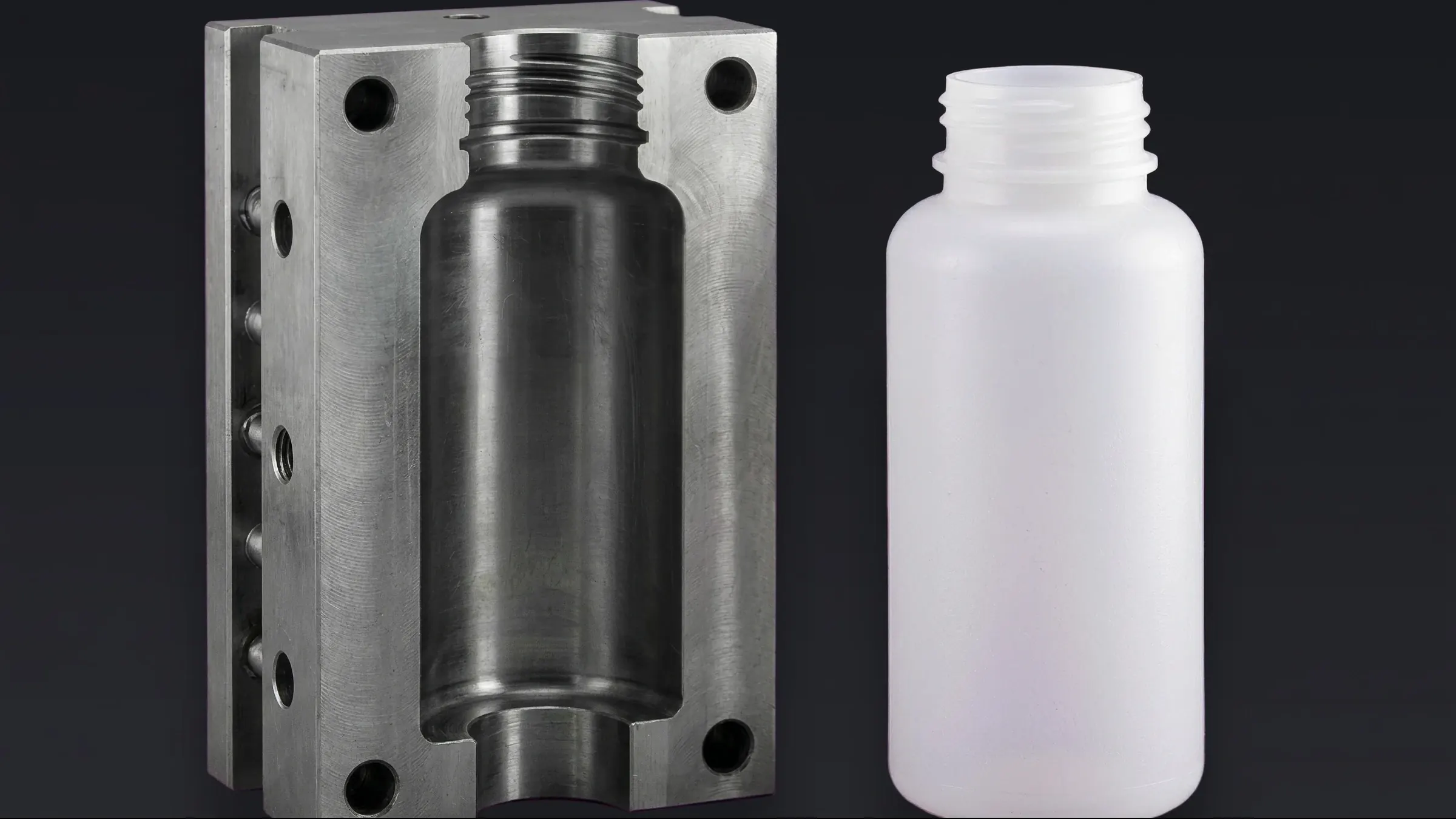 A machined steel mold block whose hollow cavity matches the shape of the bottle standing beside it